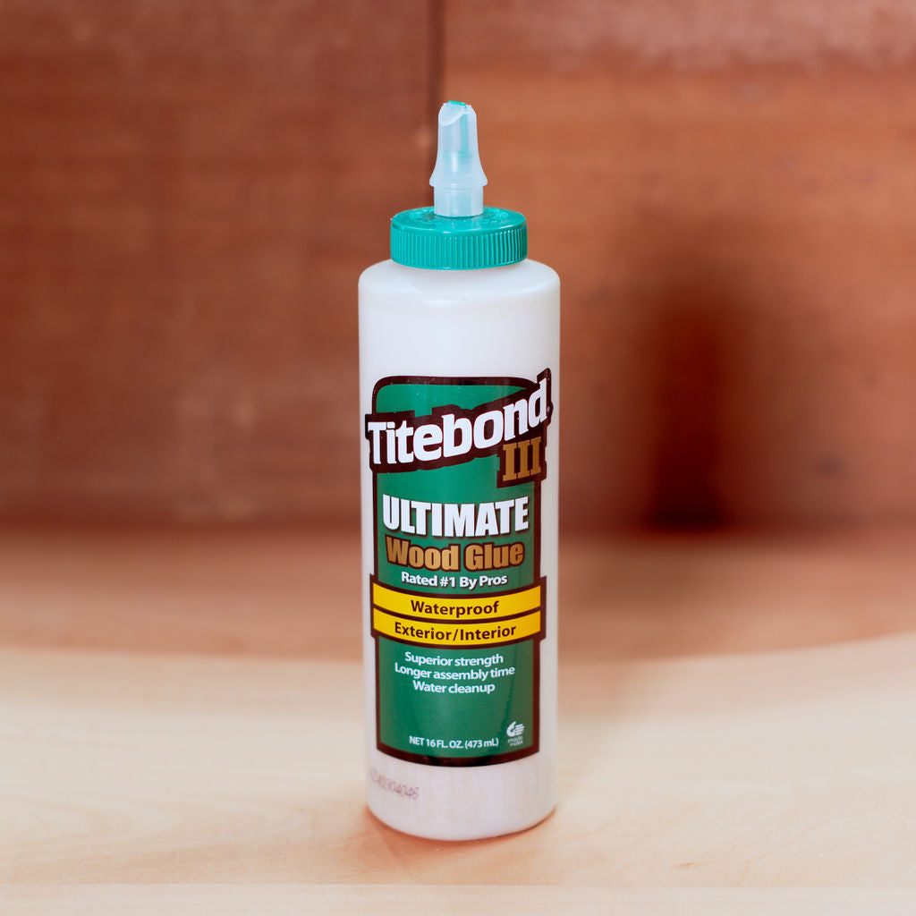 473ml bottle of Titebond III Ultimate Wood Glue on a wooden surface with a brown background